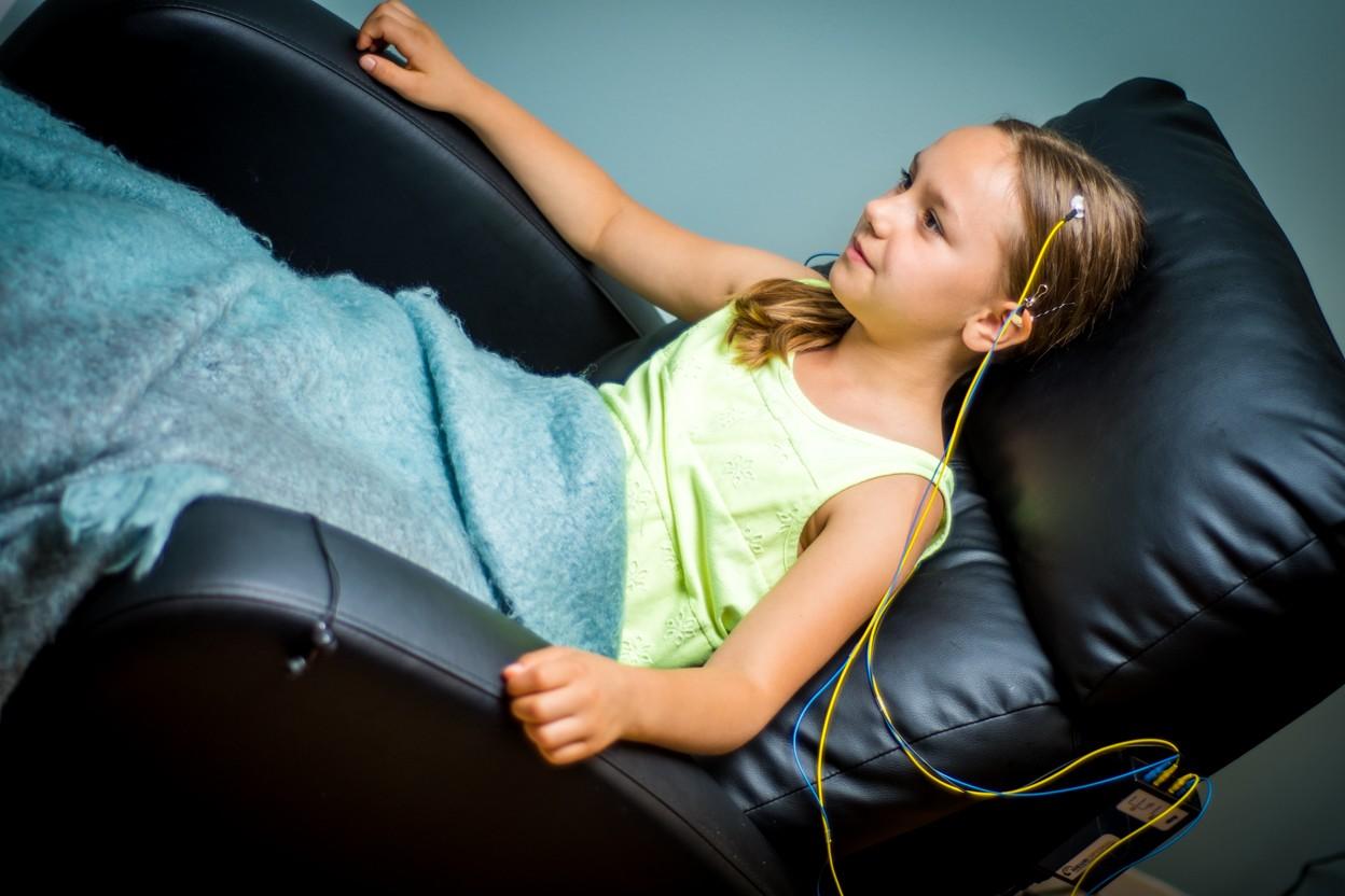A girl relaxes in a recliner under a soft blanket during a NeurOptimal brain training session